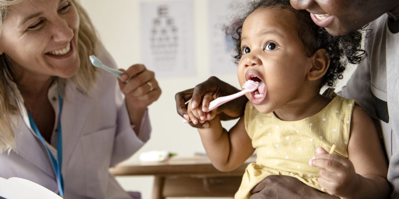 Dentist teaching a little girl how to brush her teeth