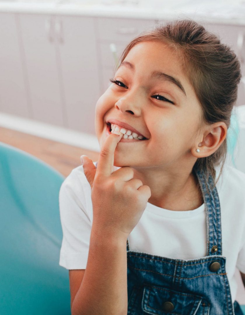 Mixed race little patient showing her perfect toothy smile while sitting dentists chair